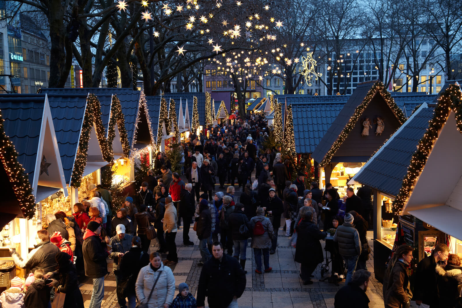 Besucher auf dem 'Markt der Engel' auf dem Kölner Neumarkt laufen an leuchtend dekorierten Buden vorbei.