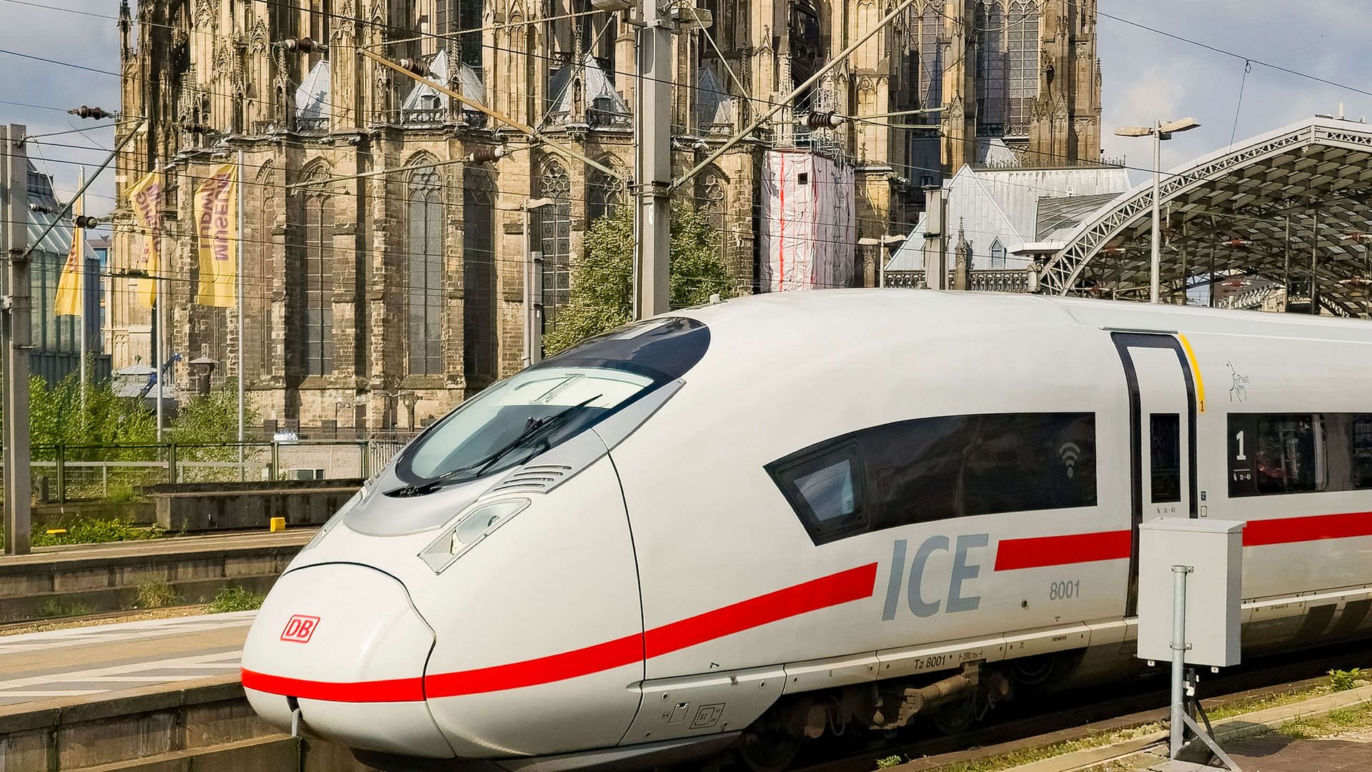 ICE am Bahnsteig vor großer gotischer Kathedrale mit Oberleitungen und Bahnhofsdach