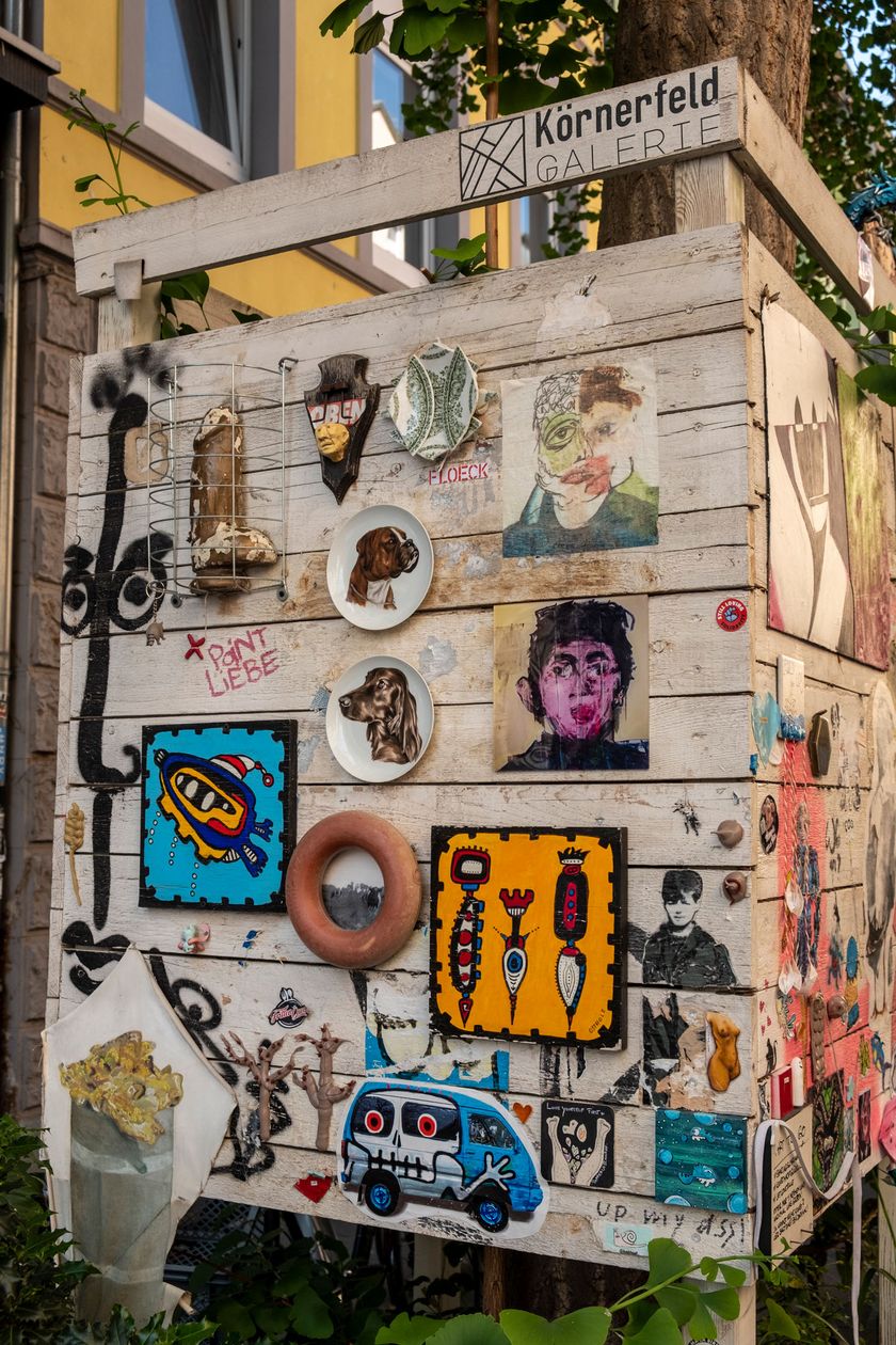 Auf einer Lattenwand sind viele verschiedene urbane Kunstwerke zusehen.