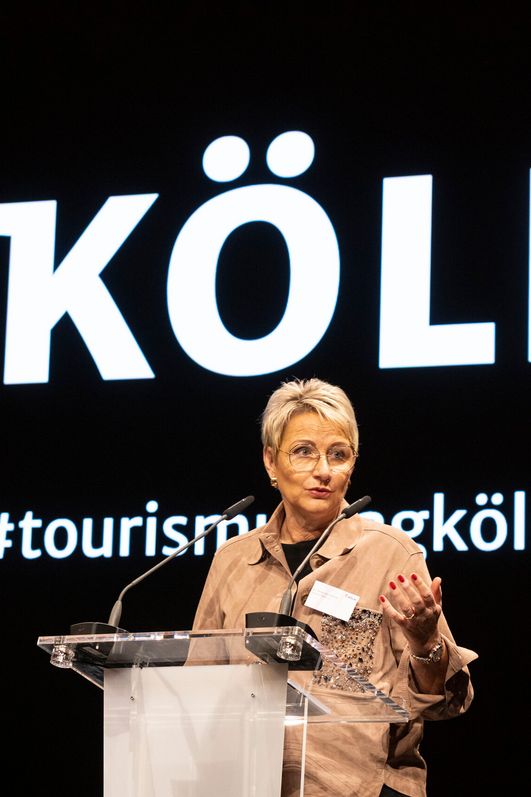 Frau Dr. Döll-König spricht vor einem Podest zu einem Publikum. 