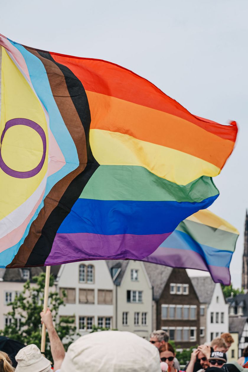 Eine bunte Fahne weht im Wind. Im Hintergrund ist die Kölner Altstadt und Dom zu sehen.