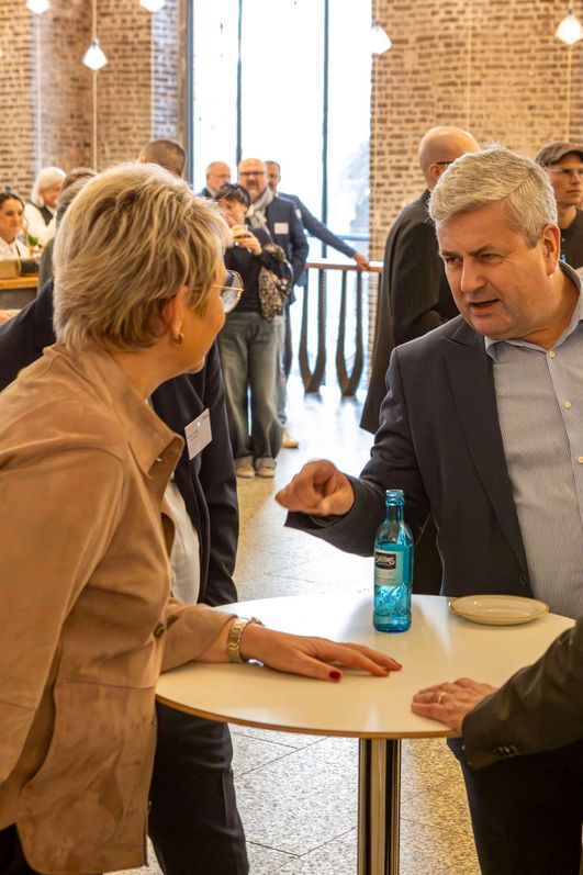 Eine Gruppe von Menschen stehen um einen runden Stehtisch und führen eine anregende Unterhaltung.