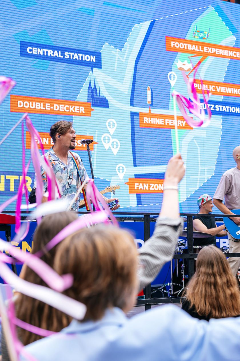 Eine Band spielt vor Publikum open air. Hinter der Band ist eine große LED-Wand mit den Umrissen von Köln und Symbolen.