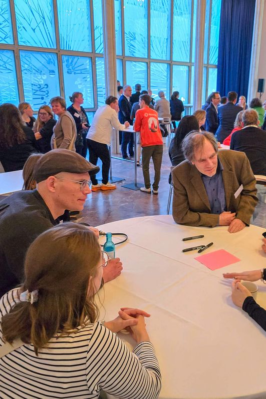 Um einen runden Stehtisch unterhaltet sich eine Gruppe von Menschen. 