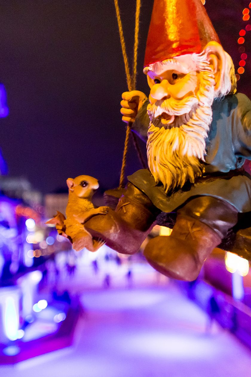 Ein festlich beleuchteter Weihnachtsmarkt mit bunter Beleuchtung, ein schaukelnder Heinzelmann in Nahaufnahme.