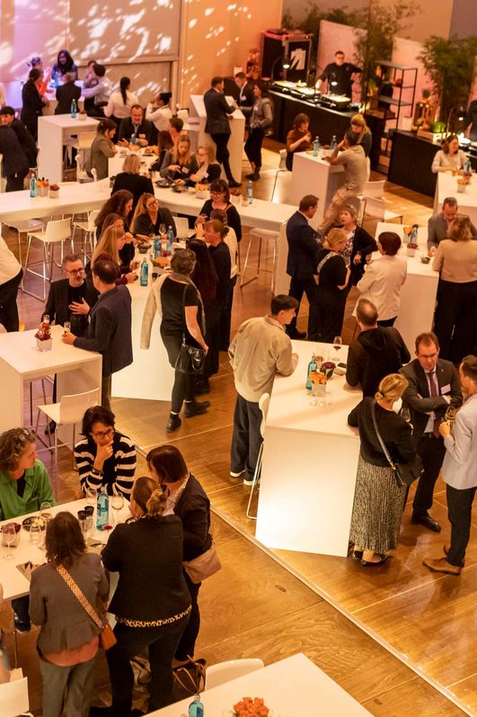 Auf dem Bild ist der Catering Bereich aus der Vogelperspektive zu sehen. Menschen unterhalten sich an Stehtischen.