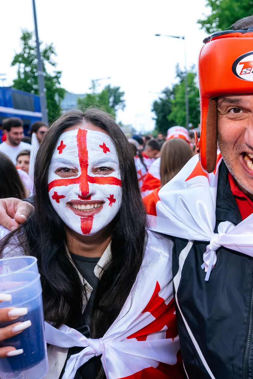 Eine Frau mit einer Gesichtsbemalung in Form einer Flagge steht lächelnd neben einem Mann, der einen Boxhandschuh in die Kamera hält. 
