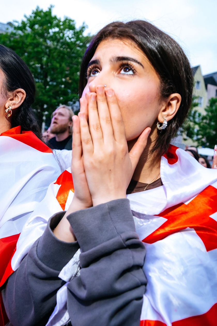 Drei Frauen mit Flaggen um die Schultern schauen gespannt in die Höhe. Eine Frau hält sich die Hände vor das Gesicht.