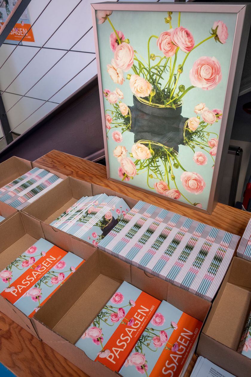 Ein Karton mit Prospekten zur den Passagen steht auf einem Tisch, dahinter ein florales Gemälde.