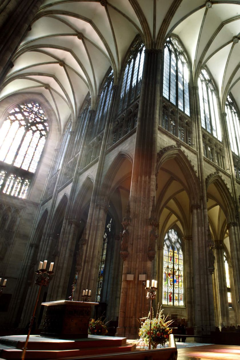 Blick über den Alter in den Innenraum vom Kölner Dom. Das Licht bricht durch die Domfenster und verleiht dem Raum eine mystische Atmosphäre. 