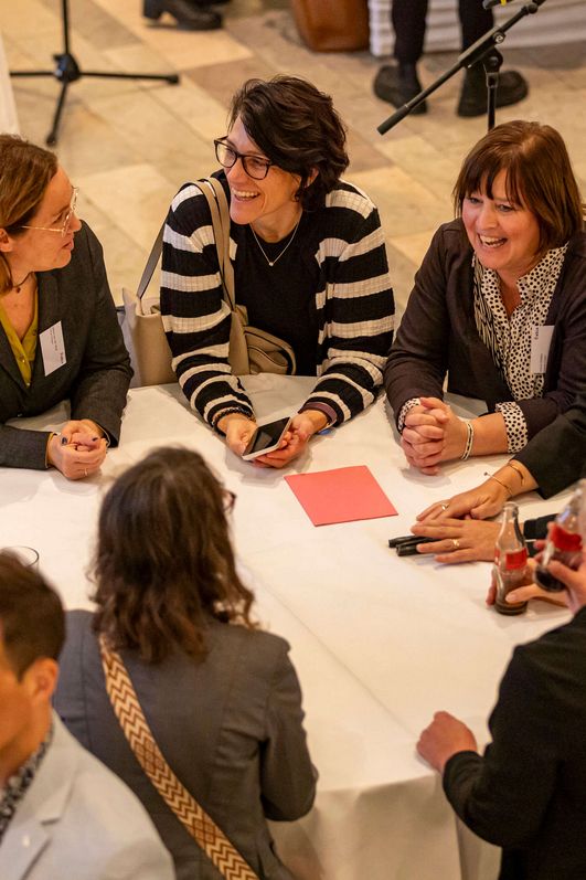 Eine Gruppe von Menschen steht um einen runden Stehtisch und hält eine fröhliche Konversation.