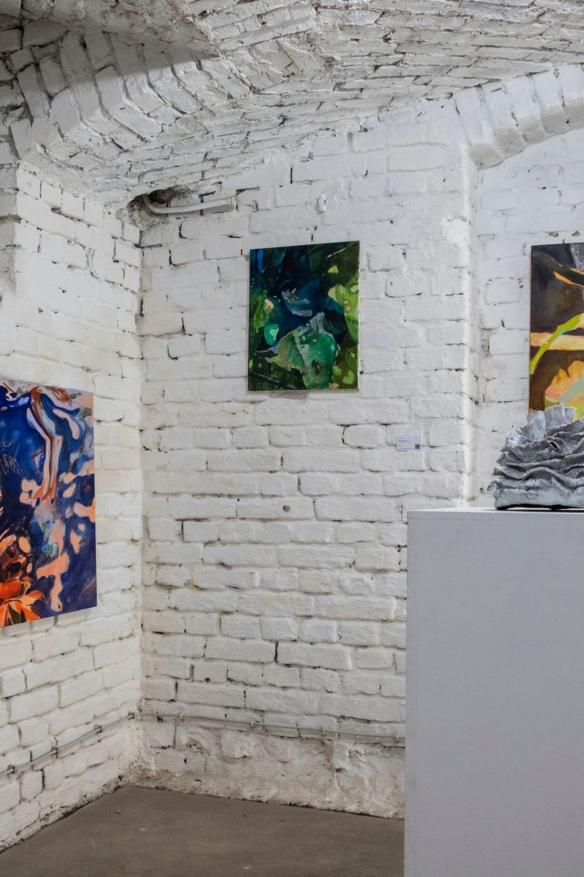 Ein Gewölbekeller mit weiß gestrichener Backsteinwand. Bunte abstrakte Gemälde hängen an den Wänden.