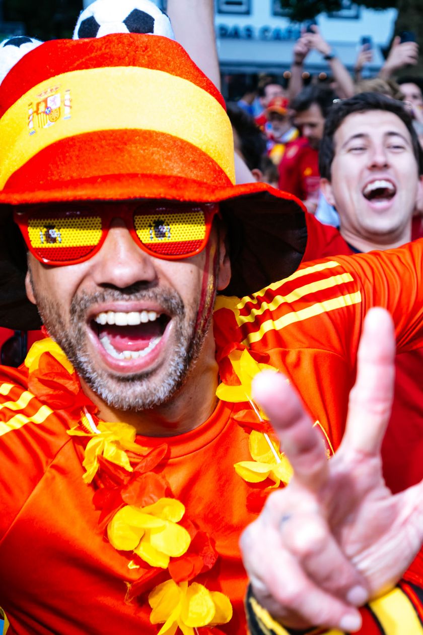 Zwei Männer mit roten Trikots, lustigen Hütten und Brillen jubeln in die Kamera und zeigen das Victory-Zeichen.