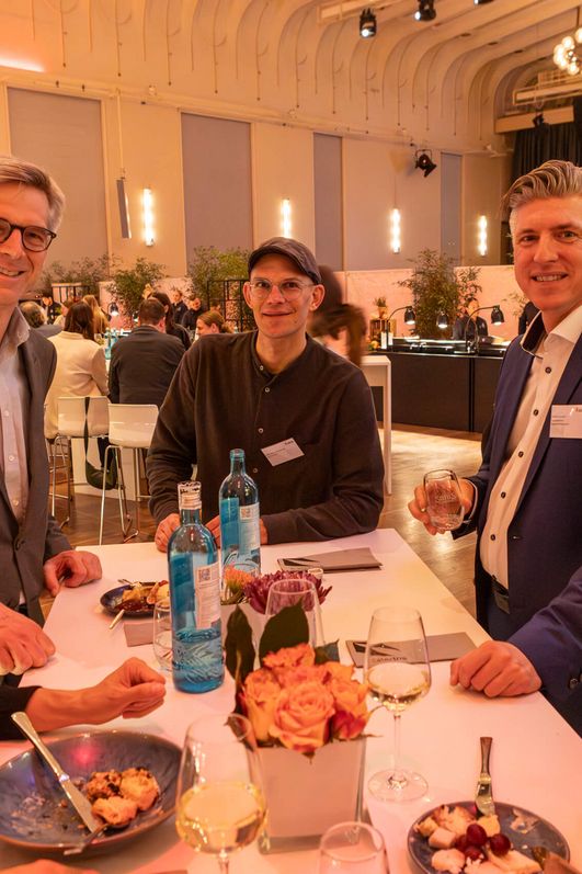 Fünf Personen stehen an einem Stehtisch und posieren lächelnd in die Kamera.