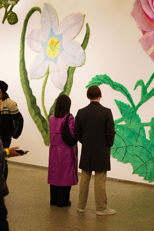 Menschen stehen in einem hellen Raum mit floralen Wandgemälden. 