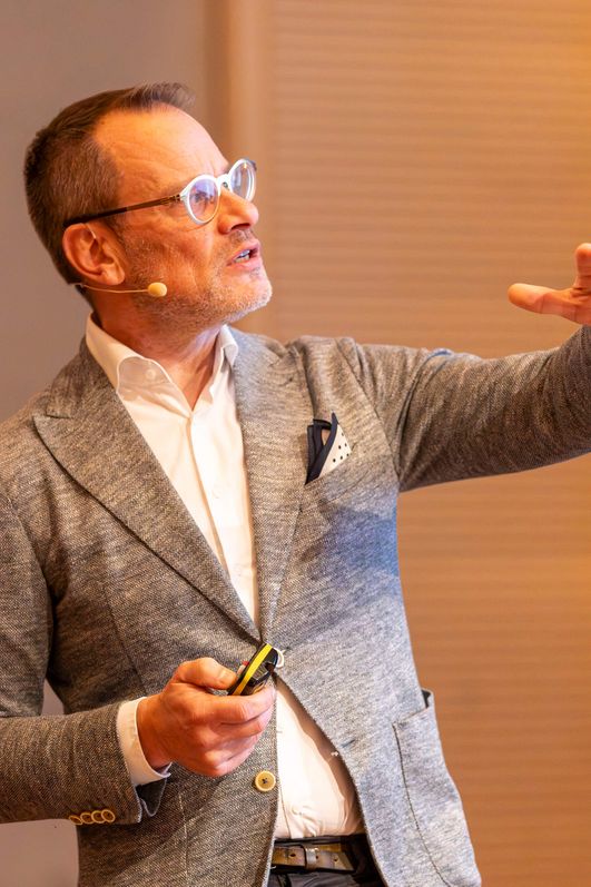 Ein Mann mittleren Alters hält fokussiert einen Vortrag, dabei gestikuliert er mit den Händen.