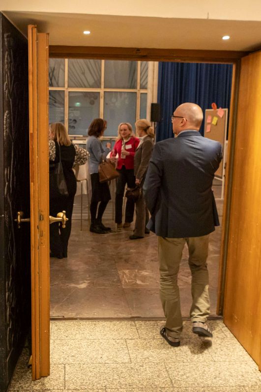 Auf dem Bild ist der Eingang zu einem Saal im Gürzenich zu sehen. Ein Mann passiert die Türschwelle und ein Bildschirm präsentiert den Titel des Themenpanels. 