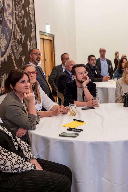 Ein Publikum hört fröhlich konzentriert bei einem Vortrag zu.