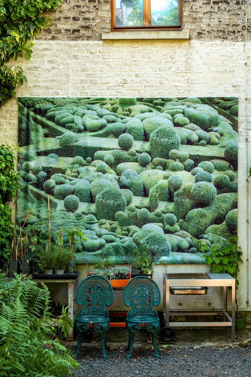 Ein großes Gemälde hängt an einer Hausfassade in einem Hinterhof. Davor sind verschiedene Möbelstücke gestellt. Die Farbe grün dominiert im Foto.